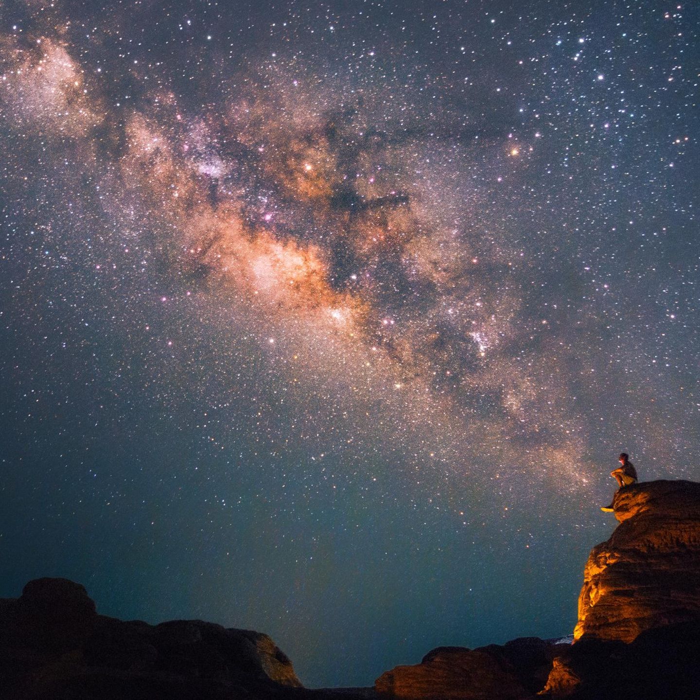 Ein Mann blickt in den Nachthimmel, wo sich die Milchstraße zeigt