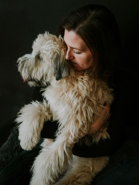 Frau umarmt weissen flauschigen Hund vor schwarzem Hintergrund