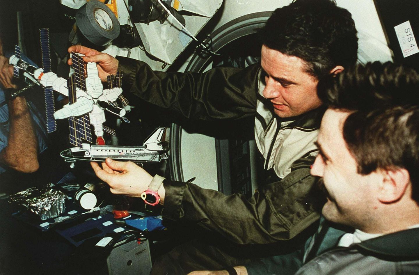 Zwei Kosmonauten halten Papiermodelle vom Shuttle Atlantis und der Raumstation Mir in der Hand