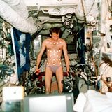 Ein Kosmonaut in Unterhose, den Oberkörper mit Punkten beklebt, führt ein Experiment durch.