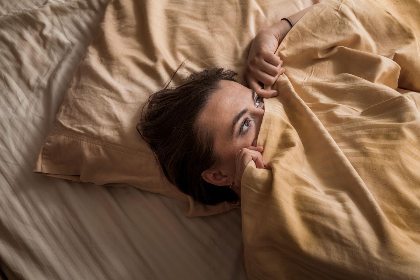 Eine Frau liegt im Bett, die Bettdecke halb über ihr Gesicht gezogen