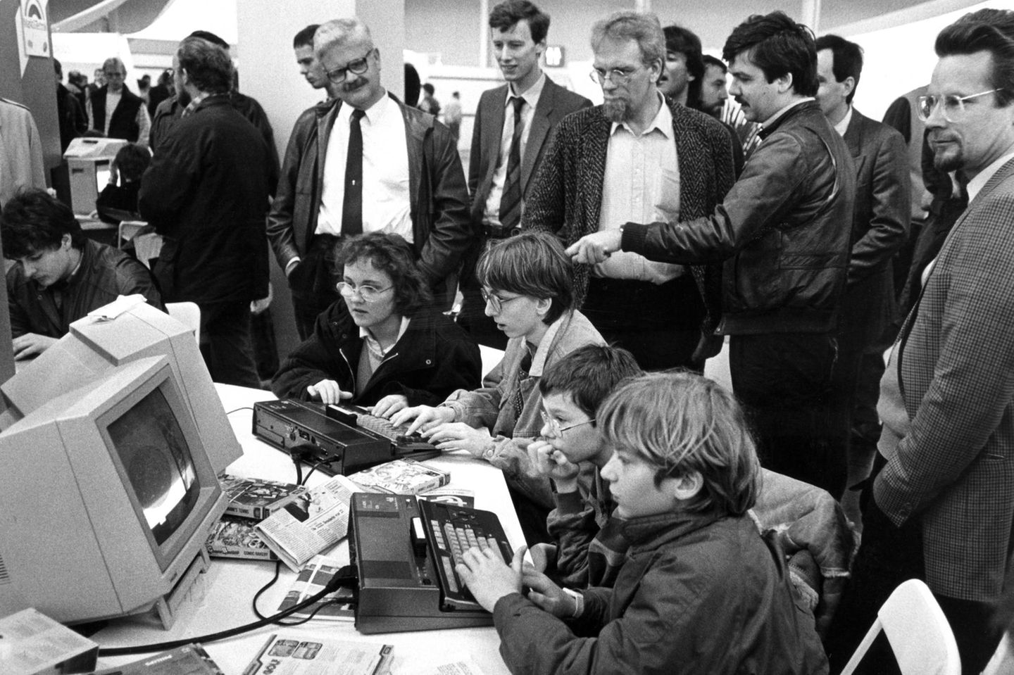 Eine Frau und mehrere Jungen bedienen Computer während Männer zuschauen