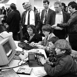 Eine Frau und mehrere Jungen bedienen Computer während Männer zuschauen