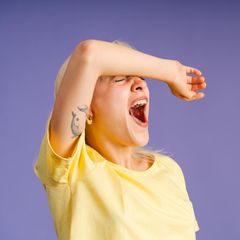 Frau vor lila Hintergrund gähnt herzhaft