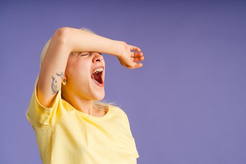 Frau vor lila Hintergrund gähnt herzhaft