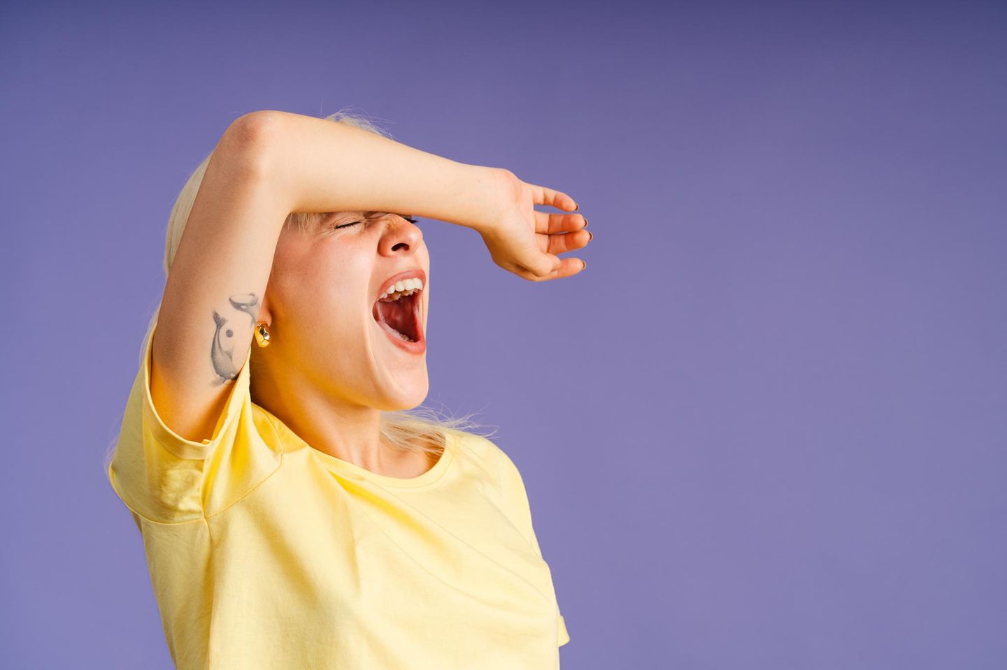 Frau vor lila Hintergrund gähnt herzhaft