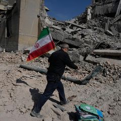 Mann trägt Iran-Fahne vorbei an Trümmern