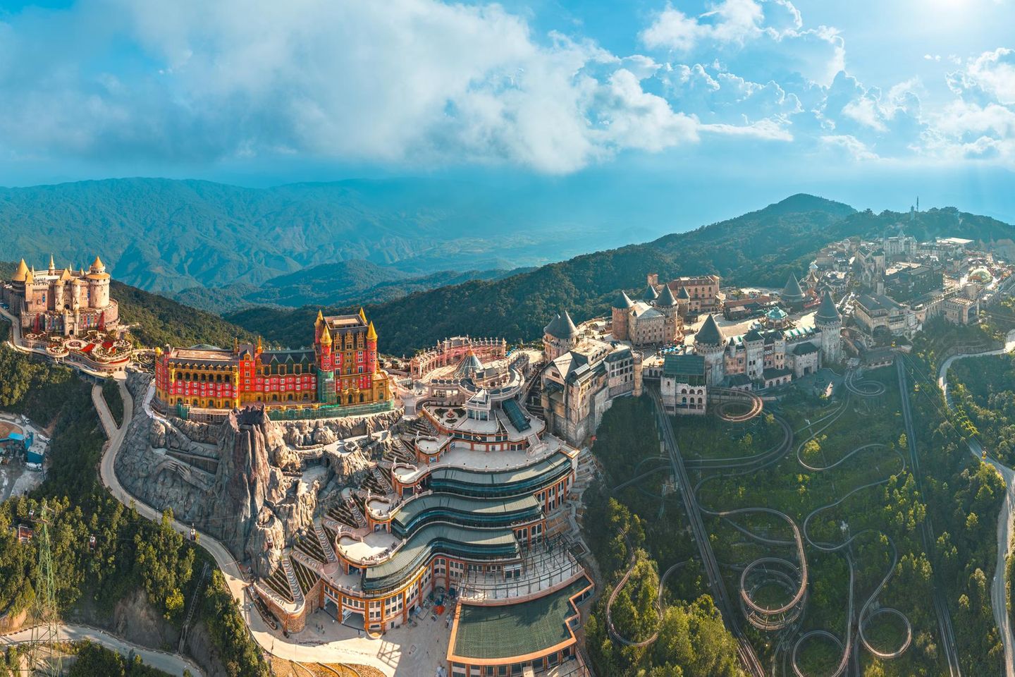 Wer mit der Gondel hoch ins Truong-Son-Gebirge schwebt, landet nicht auf einem Gipfel, sondern in einem Vergnügungspark: Ba Na Hills. Besonders stimmungsvoll ist die Auffahrt am späten Nachmittag, wenn die Sonne alles in goldenes Licht taucht und hinter den Bergen versinkt – sofern es nicht zu neblig ist. Hier oben ist das Wetter deutlich kühler und wechselhafter als an der Küste. Das Areal geht auf eine französische Hill Station mit Villen aus Kolonialzeiten zurück, die nach dem Abzug der Franzosen verfielen und in den 1990er-Jahren von wohlhabenden Vietnamesen wiederbelebt wurden. Mit dem Bau der ersten Seilbahn begann der Ausbau zu einem großen Vergnügungspark mit mittelalterlichen und Fantasy-Elementen, Fahrgeschäften und Themenrestaurants.