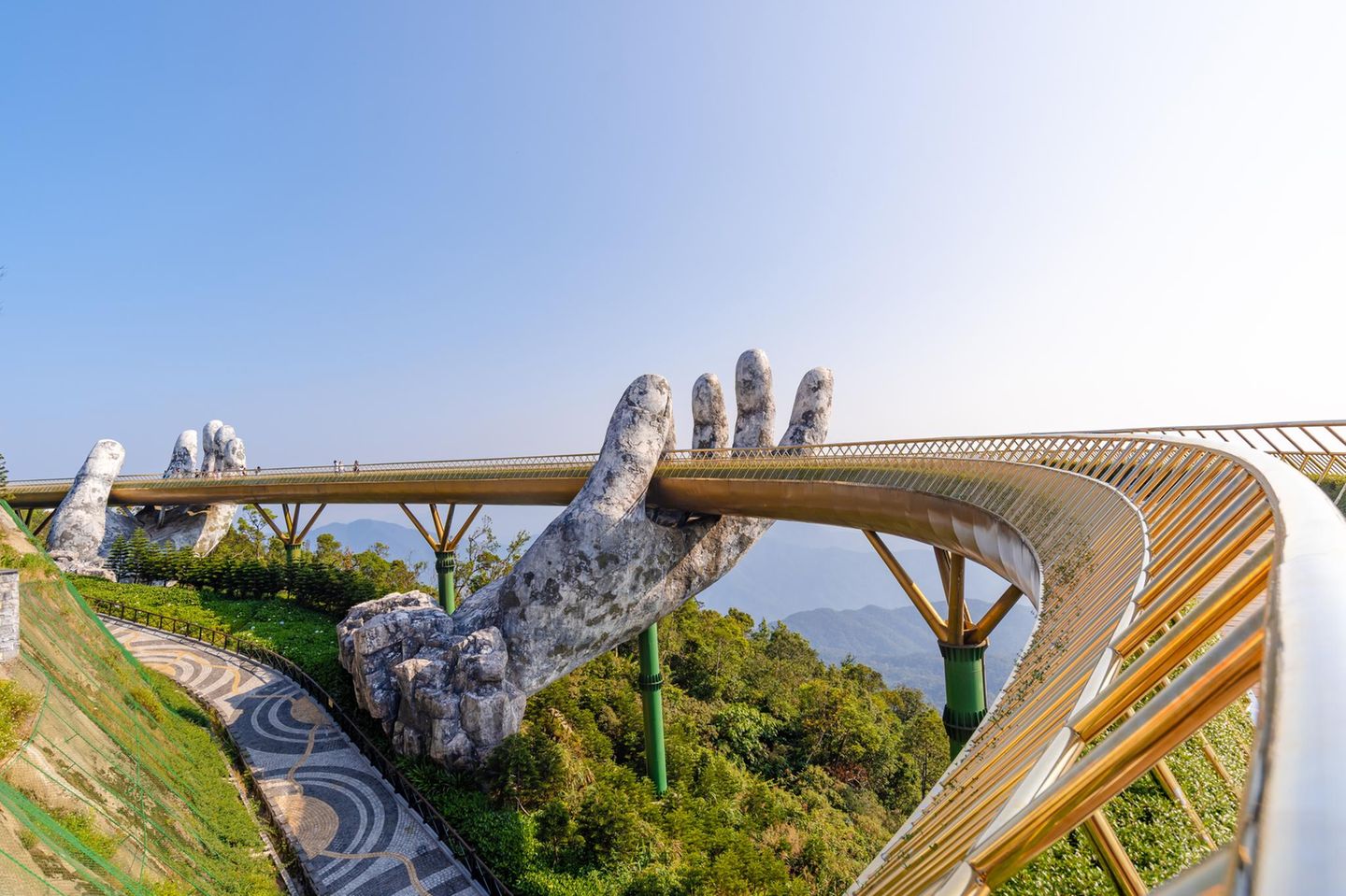 Im Land der spektakulären Brücken: Nach der steilen Seilbahnfahrt in die Ba-Na-Berge führt der Weg direkt über die Goldene Brücke in den Vergnügungspark. Die 2018 eröffnete Fußgängerbrücke scheint von zwei riesigen Steinhänden getragen zu werden – ein Motiv, das auf unzähligen Fotos landet und längst als ikonisch für Da Nang und Ba Na Hills gilt. Aber Obacht: Der Natur ist die Instagram-Romantik egal. Wegen des wechselhaften Wetters hier oben liegt die Brücke oft im Nebel. Aussicht und Hände verschwinden dann in der trüben Suppe. 