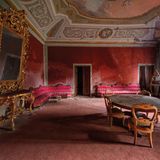 Dieses rote Wohnzimmer beherbergte einst eine italienische Arztfamilie. In dem toskanischen Palazzo ist auch das ehemalige Arbeitszimmer mit Bücherregal, Urkunden, Briefen und persönlichen Gegenständen erhalten geblieben.
