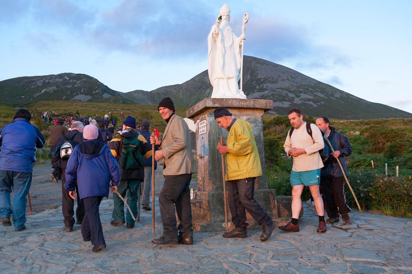 Menschen vor Statue St. Patrick, im Hintergrund Berge