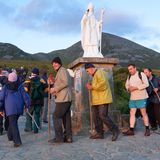 Menschen vor Statue St. Patrick, im Hintergrund Berge