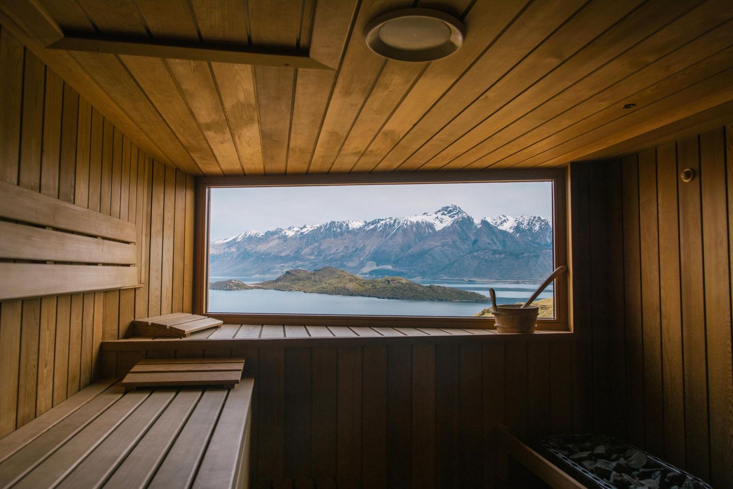Herzstück dieser Sauna ist der spektakuläre Blick auf den Lake Wakatipu und die neuseeländischen Alpen. Sie gehört zum Aro Ha Wellness Retreat, das oberhalb des Sees mitten in der Berglandschaft bei Glenorchy liegt. Entworfen wurde die rustikale Hütte vom in Wellington ansässigen Büro Tennent Brown Architects. Verbaut sind hauptsächlich natürliche Materialien wie Stein, Wolle und Holz. Dazu schmiegt sich der Bau in den Hang, als wäre er Teil der Landschaft.