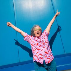 Person hebt die Arme in die Luft und steht vor einer blauen Wand