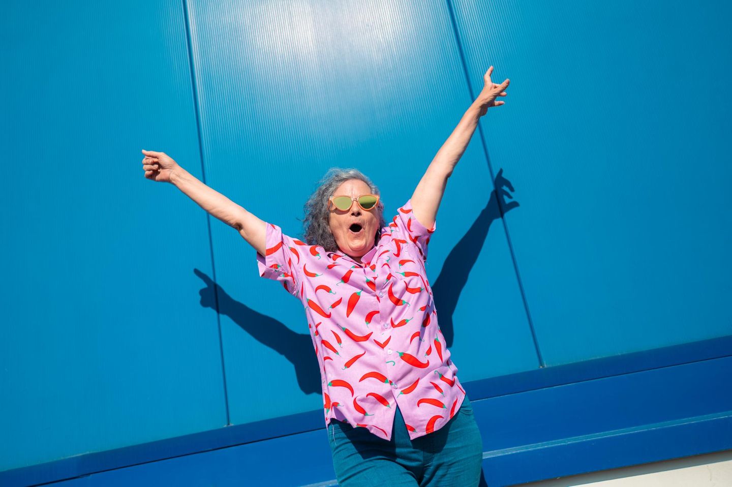 Person hebt die Arme in die Luft und steht vor einer blauen Wand