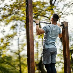 Mann macht Klimmzug im Wald an einer Stange