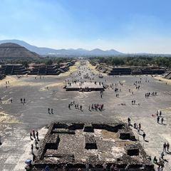 Blick über Ruinen von Teotihuacán: vorne ein Platz mit großem Podest, hinten eine von Stufenpyramiden gesäumte Straße