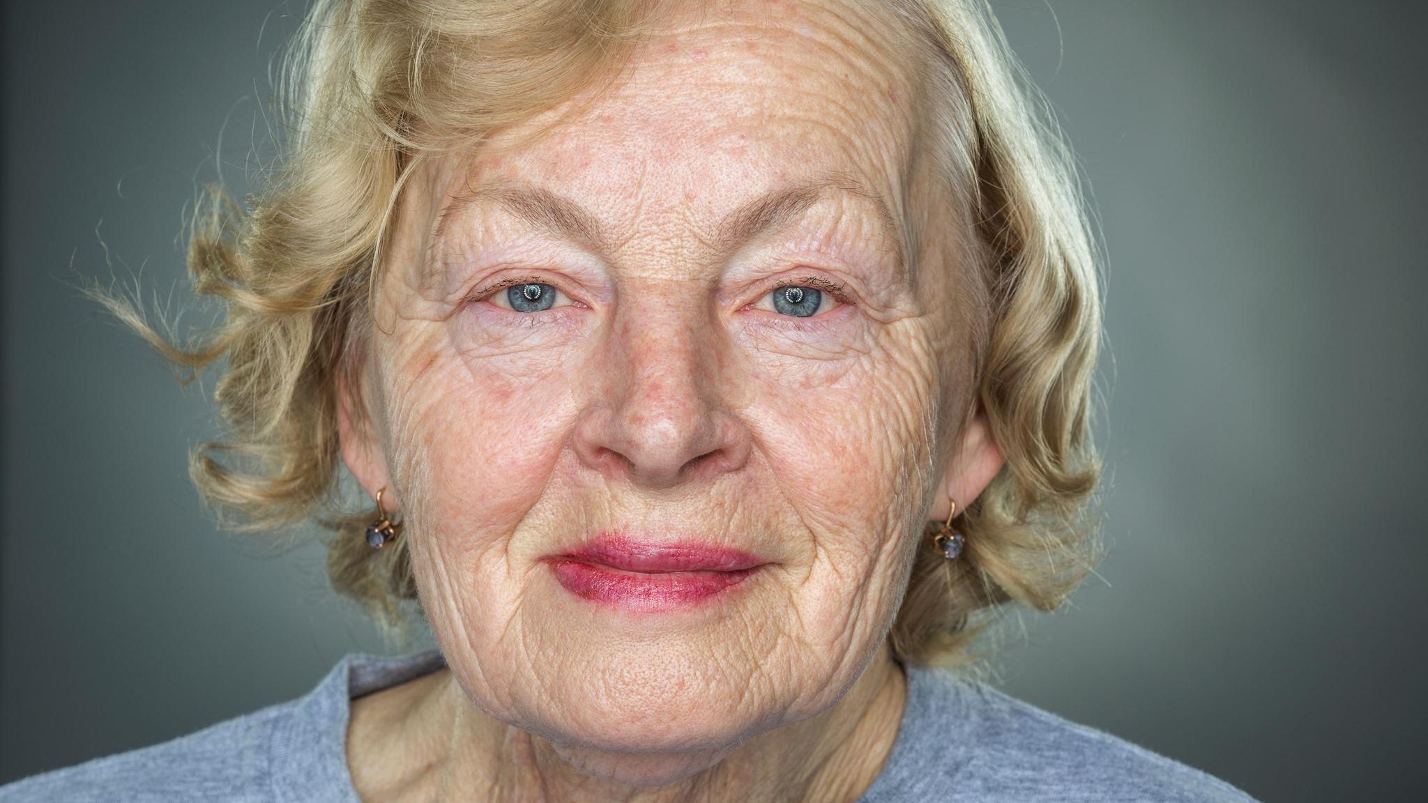 Nahaufnahme einer älteren Frau mit faltigem Gesicht vor grauem Hintergrund