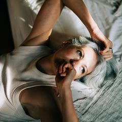 Eine Person mittleren Alters liegt auf dem Bett mit Sonnenstrahlen im Gesicht