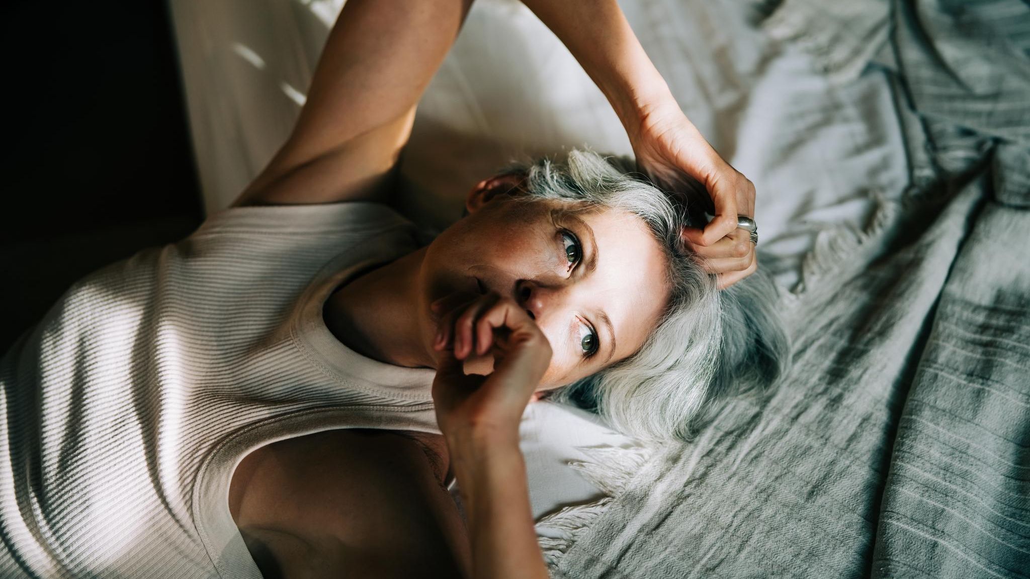 Eine Person mittleren Alters liegt auf dem Bett mit Sonnenstrahlen im Gesicht