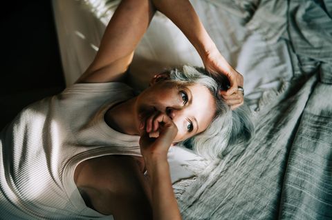 Eine Person mittleren Alters liegt auf dem Bett mit Sonnenstrahlen im Gesicht