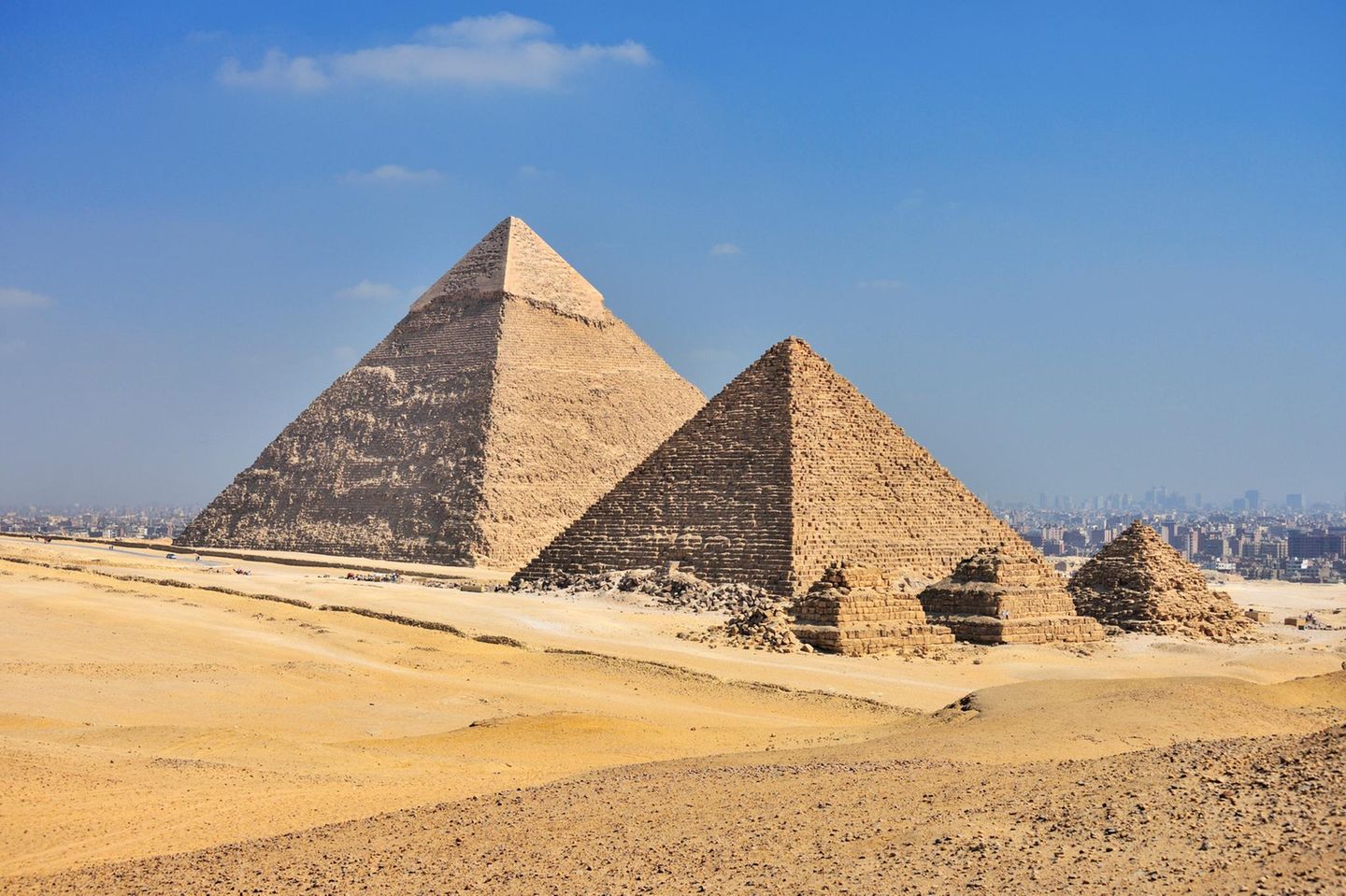 Die Pyramiden von Gizeh im Sonnenschein. Kairo zeichnet sich am Horizont im Hintergrund ab.