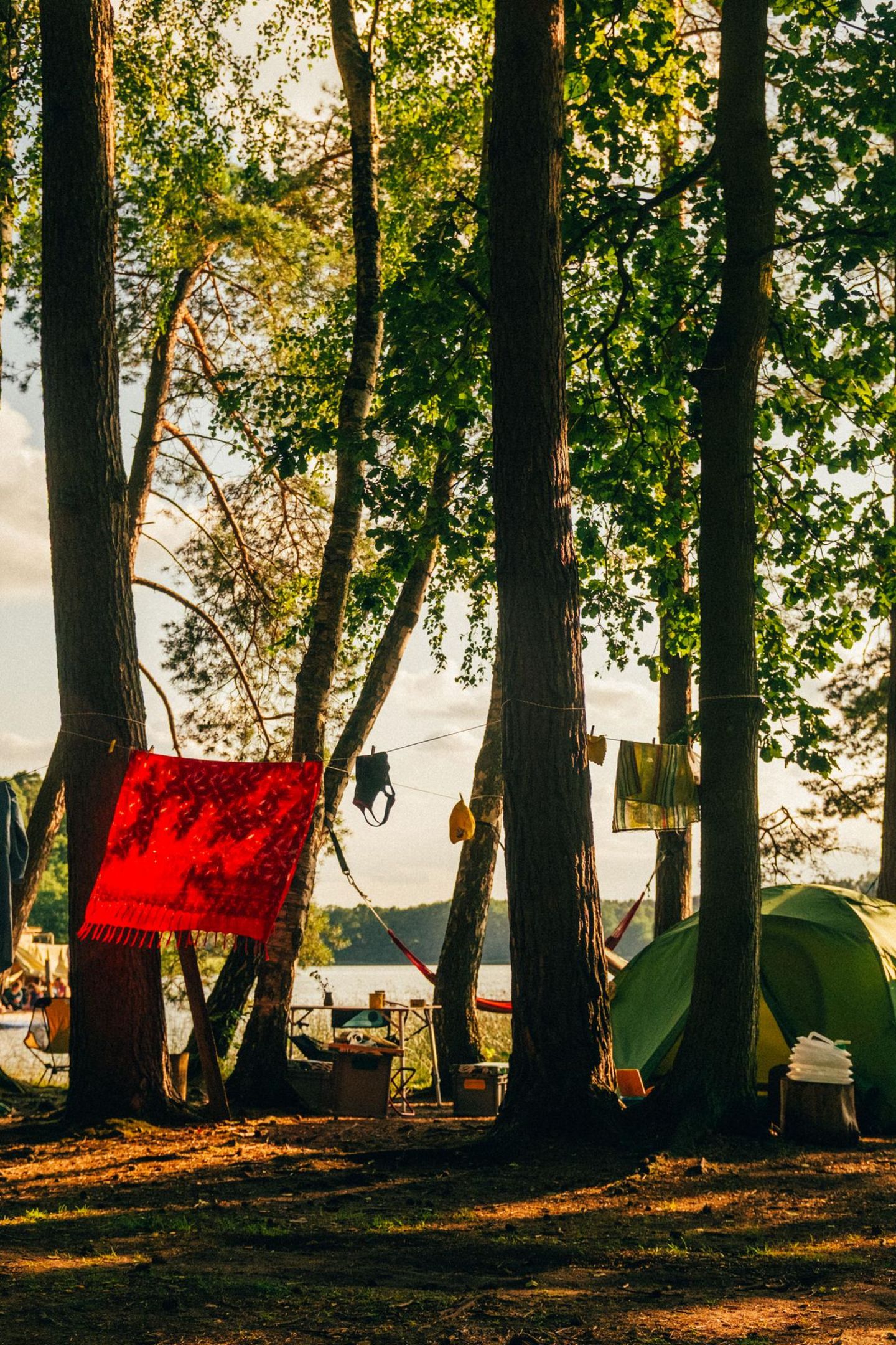 Zwischen den Bäumen spannen sich Hängematten und Wäscheleinen, bunte Zelte und Picknickdecken profitieren hier vom Schatten, während vorn der Labussee im Sonnenschein glitzert. In dessen nördlicher Bucht laden Bibertours zum Paddeln und geselligen Campen im Kiefernwald ein. Zelt vergessen? Kein Problem, ab ins Floß- oder Zelthotel. Verpflegung in Bioqualität und Campingbedarf gibt es an der Rezeption. Auf den See geht es mit geliehenem Kanu oder SUP, alternativ bringt auch eine Floßtour Spaß. Vom Zeltwald führen zwei Stege ins Wasser. Hier trifft man sich abends zum Sonnenuntergang, mit einem Teller Nudeln oder einem Buch auf dem Schoß wird es so richtig gemütlich. Danach warten Stockbrot, Sterne und Geschichten an der Feuerschale. 