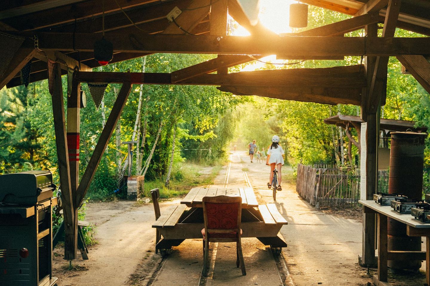 Festivalgefühl ohne Lärm: Auf sandigen Wegen folgen Gäste in der Wilden Heimat den alten Schienen, die noch über das grüne Gelände führen. Neben der Zeltwiese parken Campingbusse, dazwischen flitzen Kinder auf Kettcars über den waldigen Campingplatz. Er liegt direkt an der Siggelhavel mit kleinem Strand und Liegeweise, einem Steg und Leihkanus. Morgens bringt der Bäckerswagen frische Brötchen, samstags legt hier das Fischerboot an.