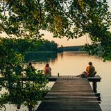 Spätnachmittags im Sommer scheint der Naturcampingplatz am Ellbogensee förmlich zu leuchten: Dann fällt die tief stehende Sonne zwischen den Kiefern hindurch und taucht Sandstrand und Steg in goldenes Licht. Zelte, Campervans, Finnhütten und kleine Holzhäuser dienen hier als sommerliche Unterkünfte. Tagsüber versorgt ein kleiner Hofladen mit Café die Gäste mit Kaffee und Gebackenem, im Seminarhaus und draußen stehen Kurse wie Yoga und Pflanzendruck auf dem Programm. Besonders Familien schlagen hier gerne ihr Lager auf, spazieren über die Wege, buddeln im Sand, platschen von der Minirutsche ins Wasser, spielen Tischkicker und rösten abends Stockbrot am Lagerfeuer. Weil der Ellbogensee direkt an der Grenze zwischen Mecklenburg-Vorpommern und Brandenburg liegt, kann man von Großmenow aus in beide Richtungen weiterschweifen – nach Norden in die Mecklenburgische Seenplatte oder nach Süden zur Nordbucht des glasklaren Stechlinsees.