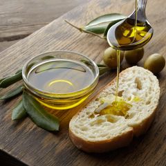 Ölivenöl tropft von einem Löffel auf ein Stück Brot