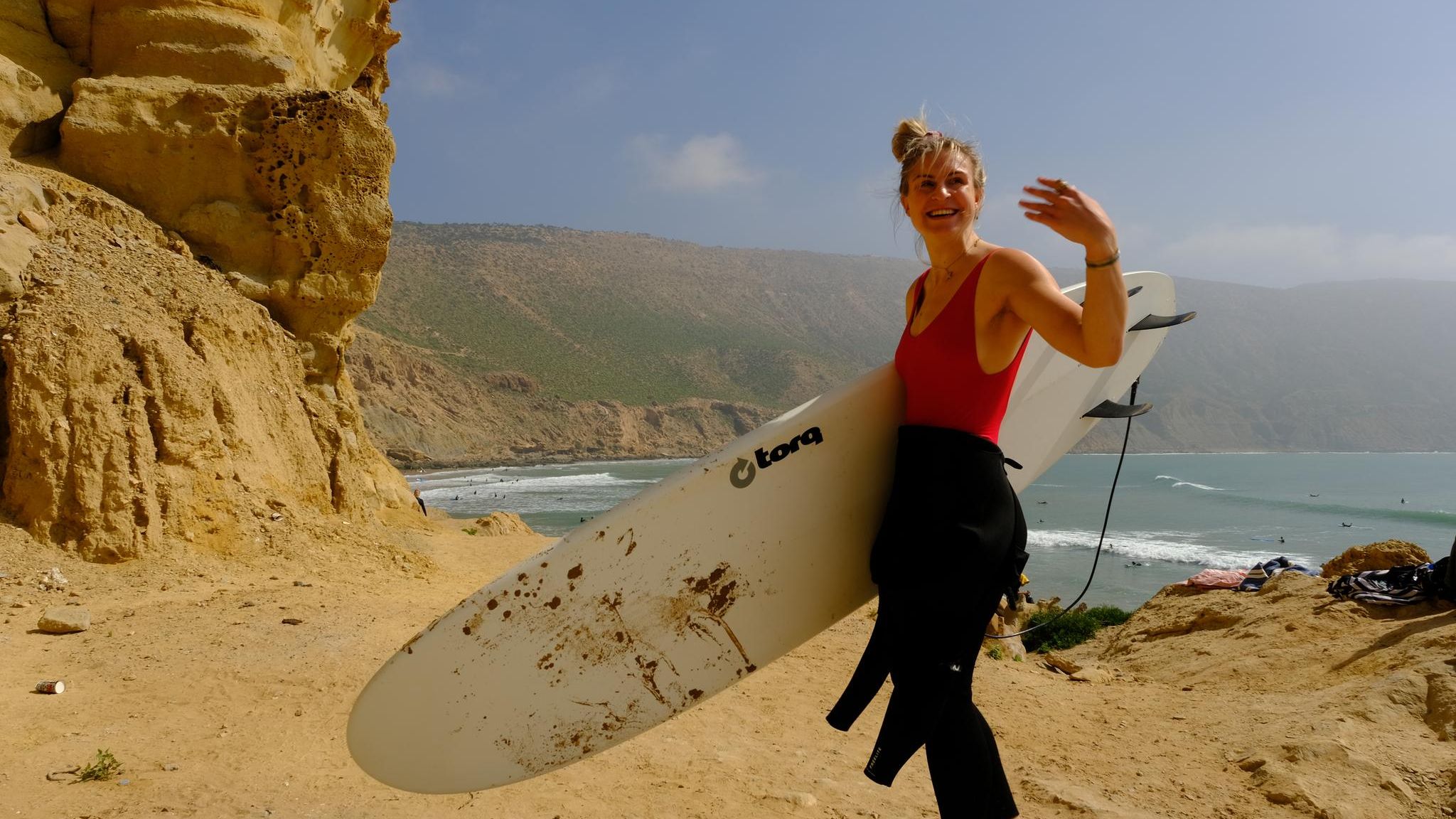 Frau mit Surfboard vor bergiger Kulisse und Meer