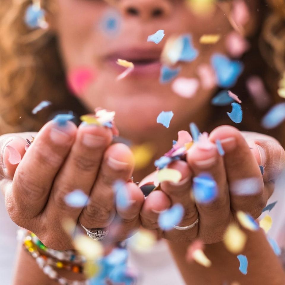 Frau pustet Konfetti aus den Händen