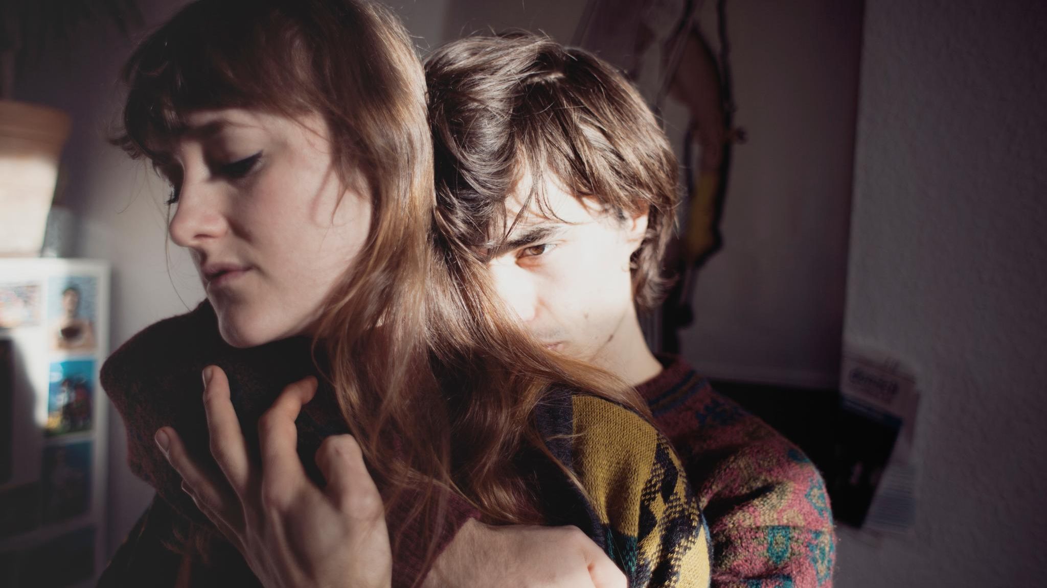 Junges Paar: Der Mann umarmt die Frau von hinten mit ernstem Blick.