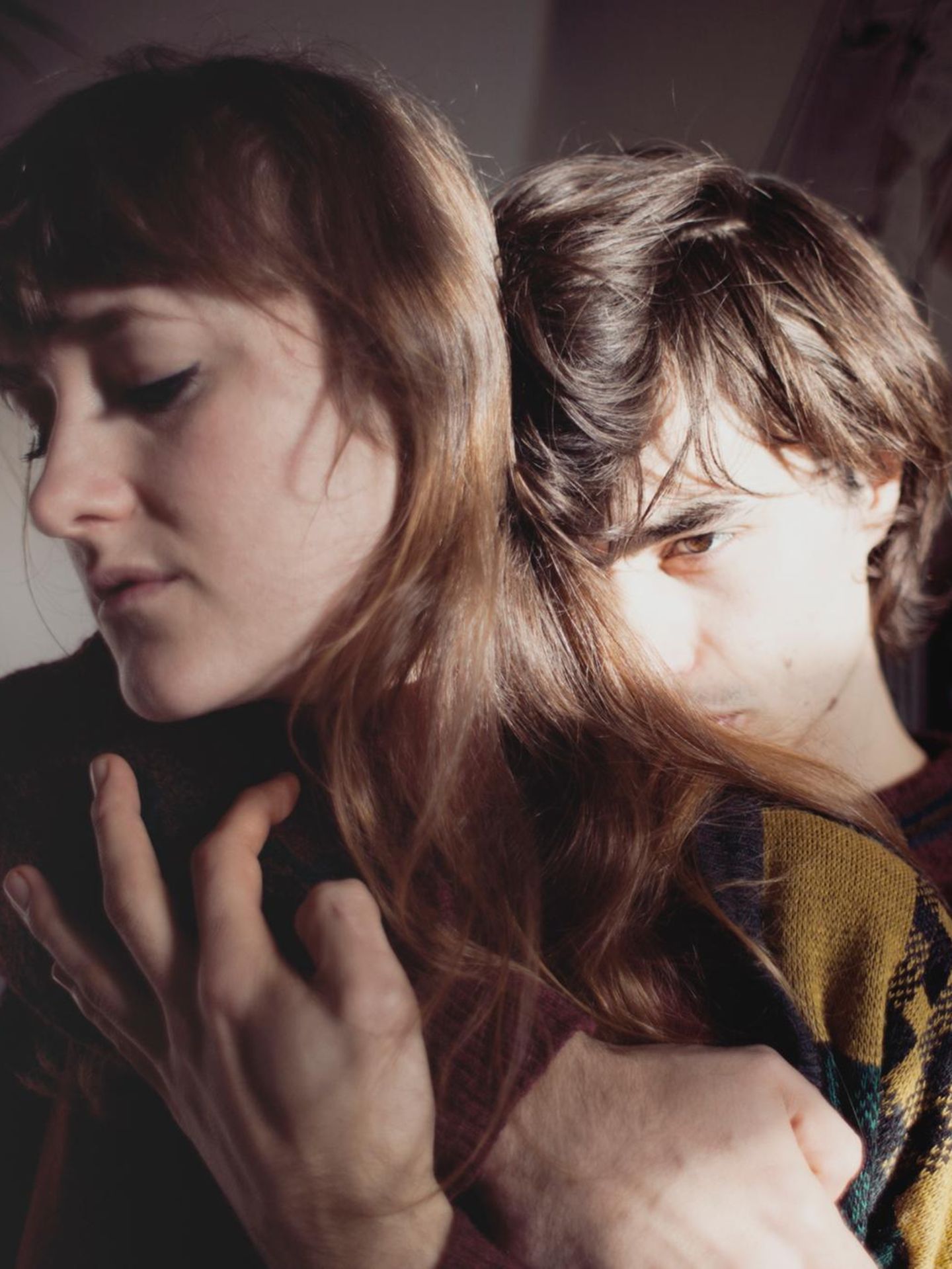 Junges Paar: Der Mann umarmt die Frau von hinten mit ernstem Blick.