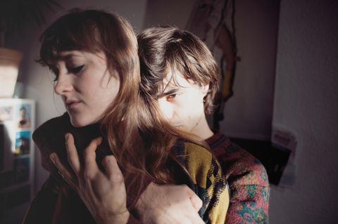 Junges Paar: Der Mann umarmt die Frau von hinten mit ernstem Blick.