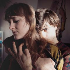 Junges Paar: Der Mann umarmt die Frau von hinten mit ernstem Blick.