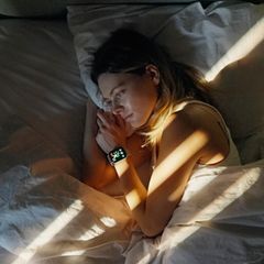 Eine Frau liegt wach im Bett, am Handgelenk eine Smartwatch