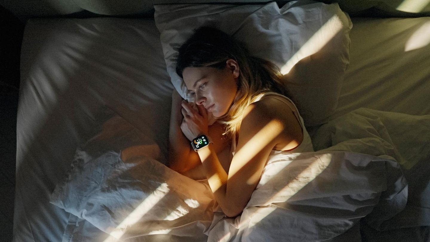 Eine Frau liegt wach im Bett, am Handgelenk eine Smartwatch