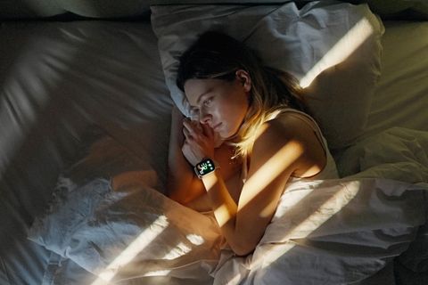 Eine Frau liegt wach im Bett, am Handgelenk eine Smartwatch