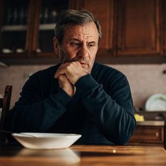 Mann sitzt nachdenklich am Tisch in der Küche