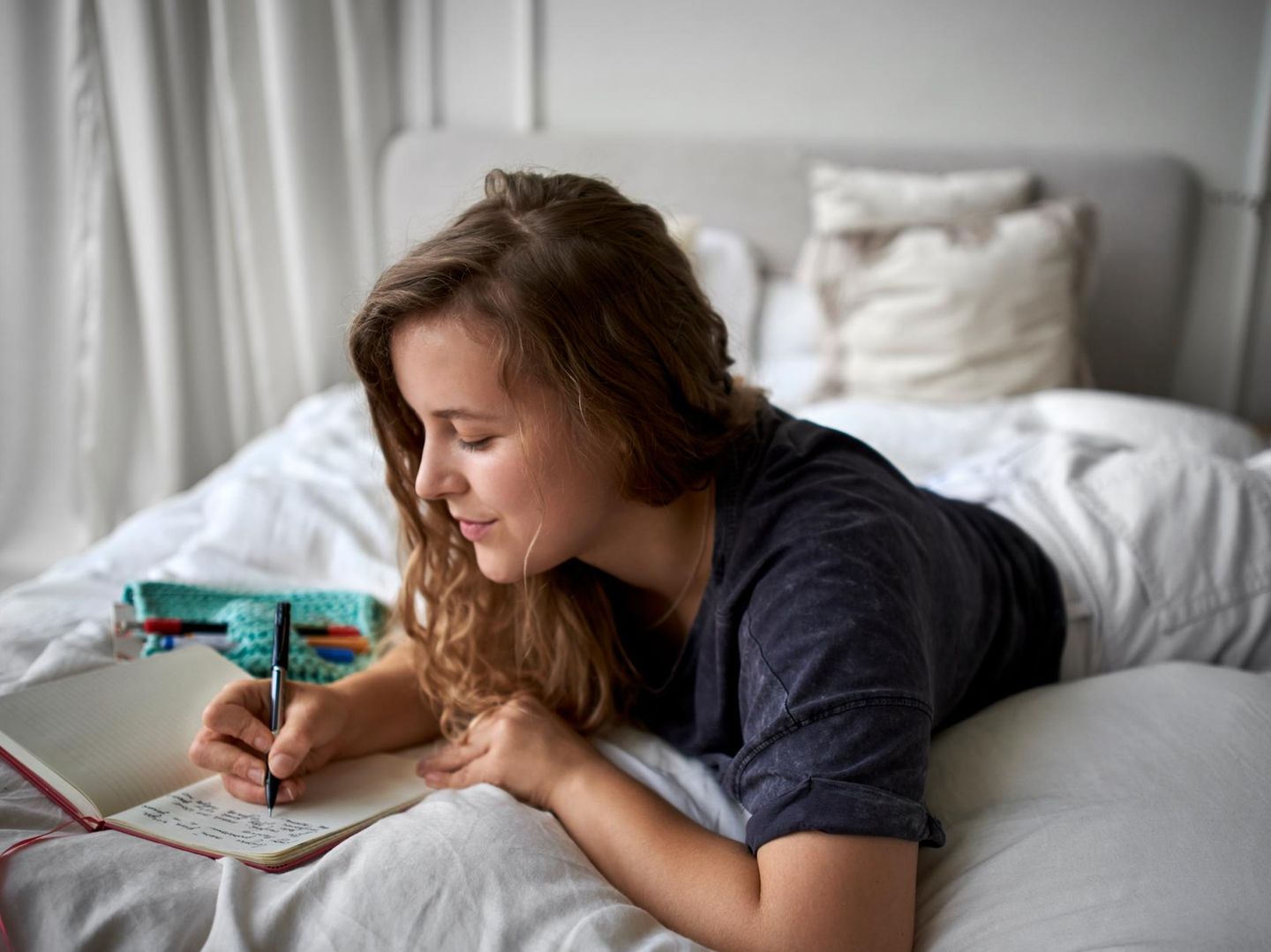 Frau liegt im Bett und schreibt in ein Buch