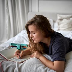 Frau liegt im Bett und schreibt in ein Buch