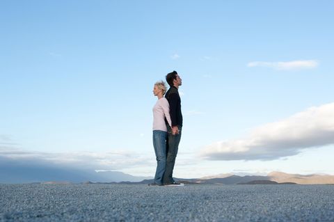Frau und Mann stehen Rücken an Rücken vor blauem Himmel