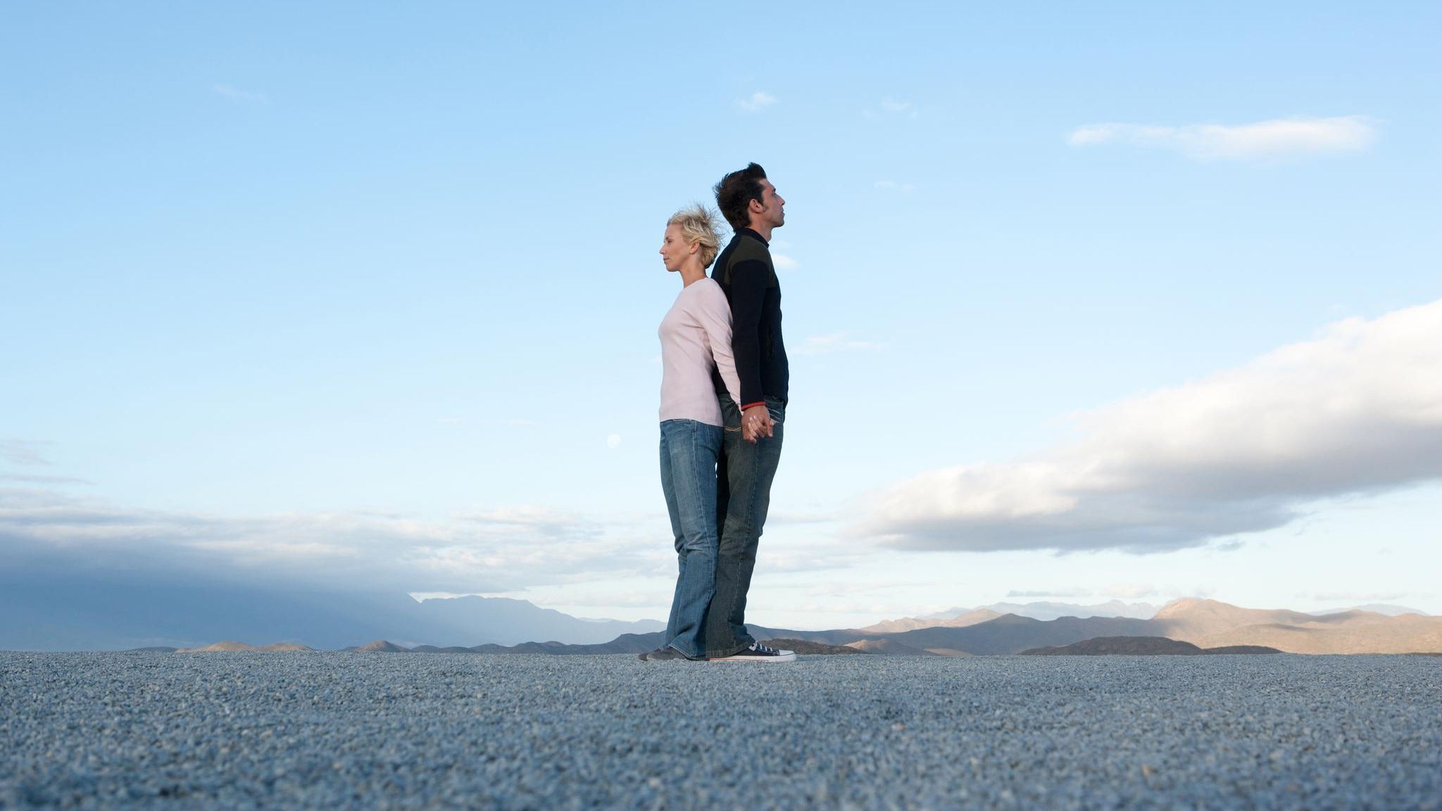 Frau und Mann stehen Rücken an Rücken vor blauem Himmel