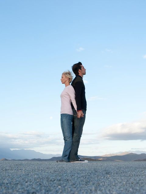 Frau und Mann stehen Rücken an Rücken vor blauem Himmel