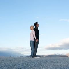 Frau und Mann stehen Rücken an Rücken vor blauem Himmel