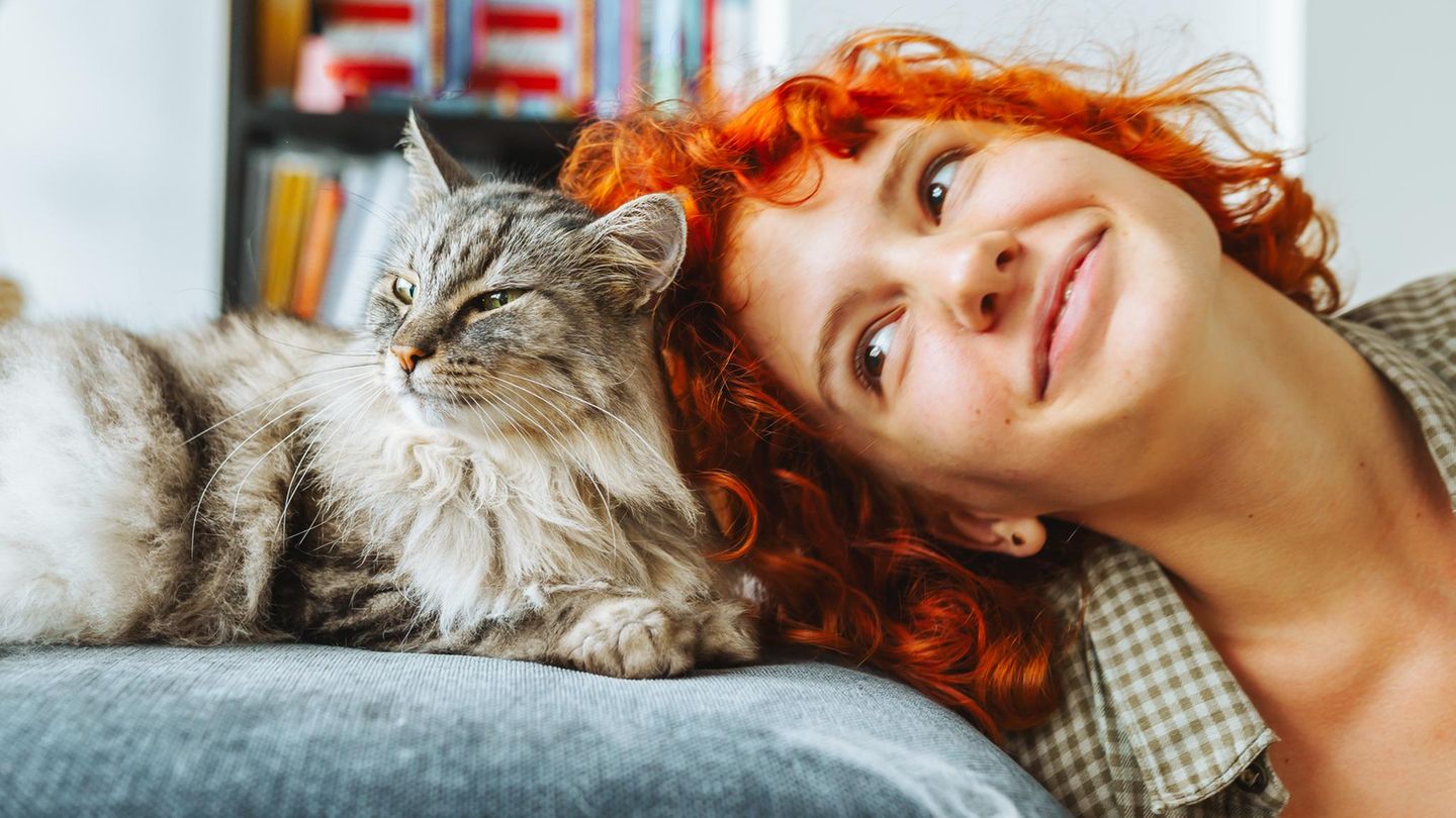 Eine rothaarige Frau kuschelt mit einer Hauskatze