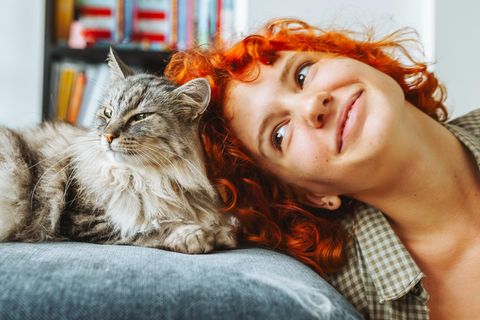 Eine rothaarige Frau kuschelt mit einer Hauskatze