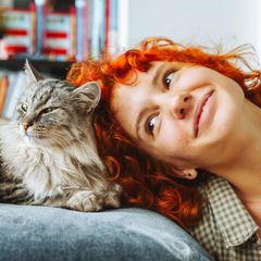 Eine rothaarige Frau kuschelt mit einer Hauskatze