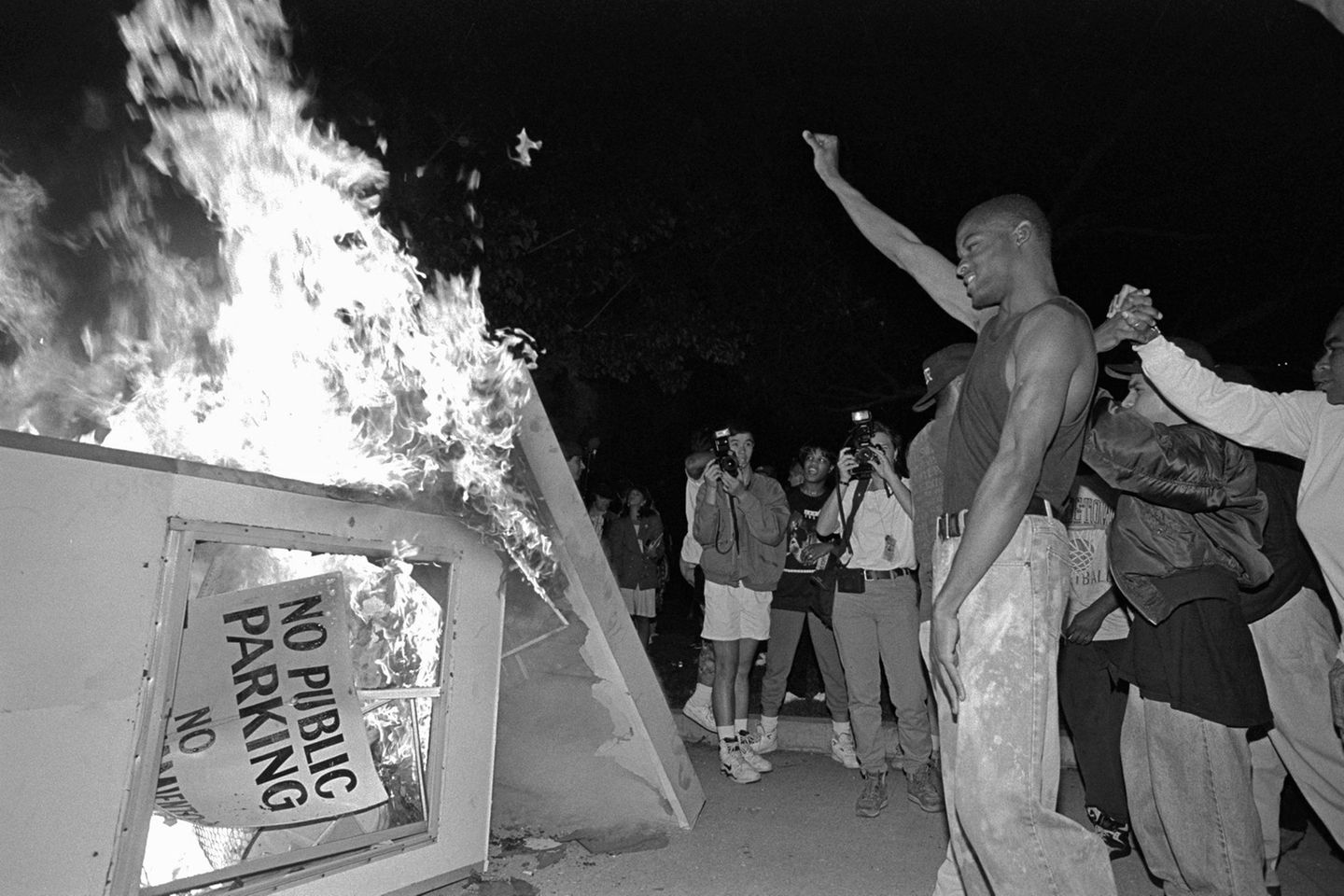 Ein Mann reckt seine Faust in die Höhe, vor ihm brennt ein Kiosk